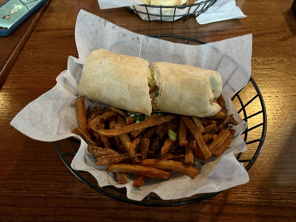 Photo of a veggie wrap with fries, in a basket on a table.